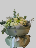 Elegant ivory bouquet with white roses, hydrangeas, eucalyptus, and seasonal flowers wrapped in sage green paper.