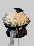 Luxury graduation bouquet with white roses, spray roses, baby's breath, black wrapping, satin ribbons, and graduation cap topper