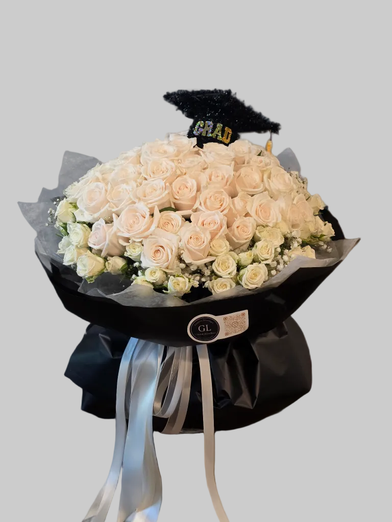 Luxury graduation bouquet with white roses, spray roses, baby's breath, black wrapping, satin ribbons, and graduation cap topper