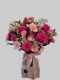 Pink floral arrangement with roses, lilies, gerbera daisies, carnations, and baby's breath in a glass vase with a pink ribbon.