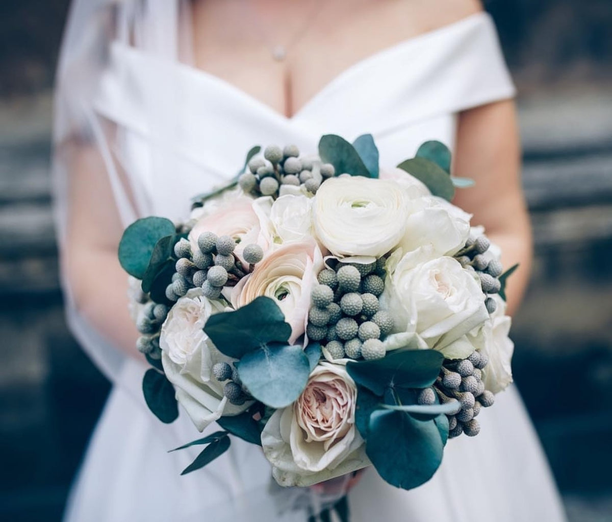 Bride holding a white and blush ranunculus wedding bouquet with eucalyptus